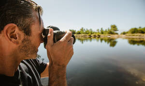 Nahaufnahme eines reifen Mannes, der mit einer DSLR-Kamera einen See fotografiert. Männlicher Fotograf, der einen See fotografiert. - JLPSF14725