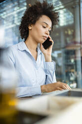 Geschäftsfrau, die im Büro mit einem Smartphone telefoniert - DIGF19052