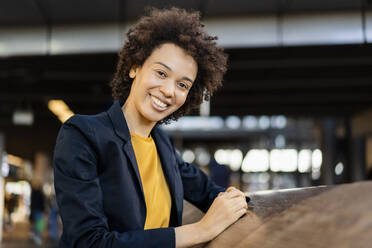 Happy businesswoman with curly hair leaning on railing - DIGF19099