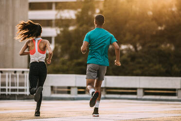 Rear view of a man and woman running together in morning. Friends in sportswear jogging together in the city. - JLPSF14743