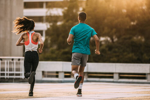 Rückansicht eines Mannes und einer Frau, die am Morgen zusammen laufen. Freunde in Sportkleidung joggen zusammen in der Stadt. - JLPSF14743