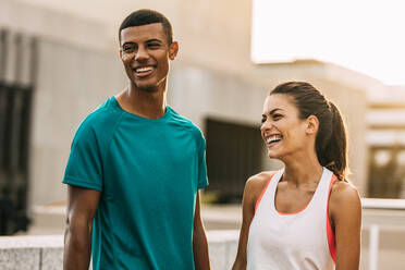 Outdoor shot of two people taking a break after running training session. Man and woman standing in the city and relaxing after a workout. - JLPSF14746