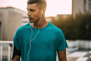 Fitness-Mann mit Kopfhörern, der nach dem morgendlichen Training Musik hört. Männlicher Sportler, der eine Pause vom Training in der Stadt macht. - JLPSF14747