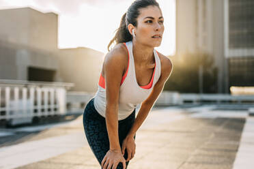 Sportlerin, die sich mit den Händen auf den Knien nach vorne lehnt und wegschaut. Läuferin, die nach dem Morgenlauf eine Pause macht. - JLPSF14752