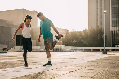 Fitness-Mann und -Frau dehnen sich gemeinsam im Freien. Zwei Menschen trainieren morgens in der Stadt. - JLPSF14757