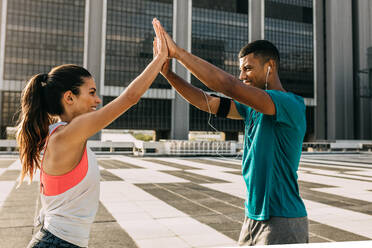 Sporty man and woman giving each other a high five while exercising outdoors. Couple giving each other a high five during their workout in the city. - JLPSF14759