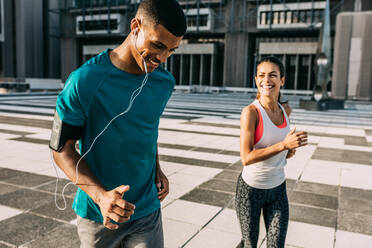 Lächelnder Mann und lächelnde Frau beim morgendlichen Lauf. Zwei Menschen in Sportkleidung beim gemeinsamen Training in der Stadt. - JLPSF14760