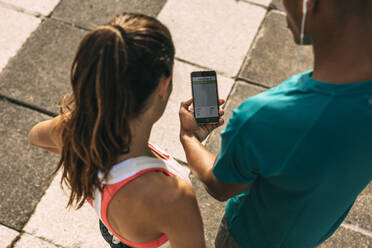 Ein männlicher und eine weiblicher Läufer, die eine Fitness-App auf ihrem Mobiltelefon benutzen, und Fitnesssportler, die die Zusammenfassung ihres Laufs auf ihrem Smartphone überprüfen. - JLPSF14763