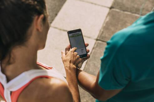 Nahaufnahme von zwei Fitness-Leuten, die die Zusammenfassung ihres Laufs auf dem Mobiltelefon überprüfen. Mann und Frau, die eine Fitness-App auf ihrem Smartphone benutzen. - JLPSF14764