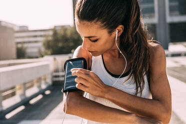 Woman listening to music with earphones from her smart phone while exercising in the city. Female in sportswear using a smartphone to monitor her progress. - JLPSF14769