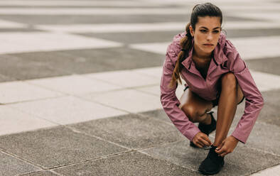 Sporty woman tying her shoes before going for a jog outside during the day. Fitness woman fastening her sport shoe lace while exercising in the city. - JLPSF14779