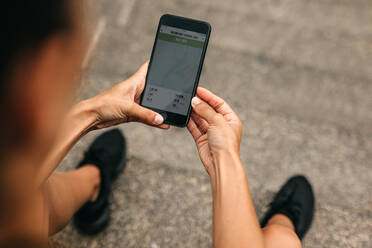 Blick über die Schulter einer Läuferin, die eine Fitness-App auf ihrem Handy benutzt. Fitness-Frau, die die Zusammenfassung ihres Laufs auf ihrem Smartphone überprüft. - JLPSF14782