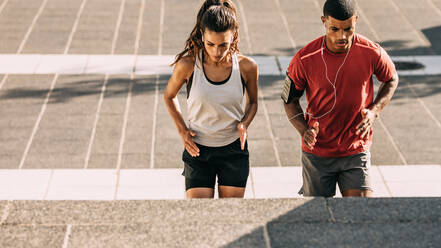 Ein Paar in Sportkleidung trainiert zusammen in der Stadt. Ein sportlicher Mann und eine sportliche Frau trainieren zusammen auf Stufen in der Stadt. - JLPSF14784