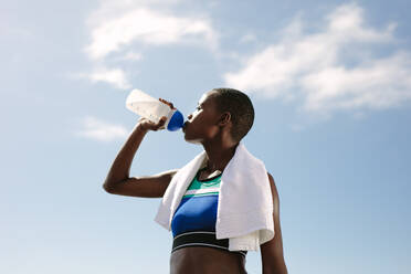 Fitness Frau trinkt Wasser gegen den Himmel. Weibliche Athletin trinkt Wasser im Freien nach dem Training. - JLPSF14793