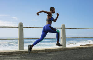 Ganzkörperaufnahme einer Frau, die auf einer Küstenstraße läuft. Eine fitte Sportlerin sprintet am Morgen auf der Strandpromenade. - JLPSF14806