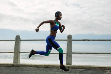 Seitenansicht Bild von fit und junge Frau läuft und übt am Morgen auf der Straße am Meer. weibliche Läuferin trainiert am Morgen. - JLPSF14807