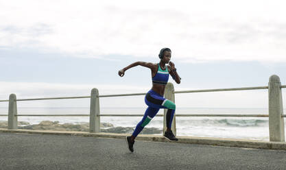 Athletic woman running on seaside promenade. Full length shot of a female runner sprinting outdoors. - JLPSF14808