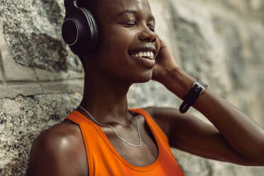 Nahaufnahme einer Frau, die nach dem Training im Freien eine Pause einlegt und dabei Musik hört. Sportlerin mit Kopfhörern, die sich nach dem Training an einer Wand entspannt - JLPSF14815