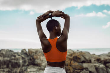 Rückansicht einer afrikanischen Frau beim Fitnesstraining. Frau in Fitnesskleidung macht Dehnübungen mit über den Kopf gehobenen Armen am Strand. - JLPSF14822