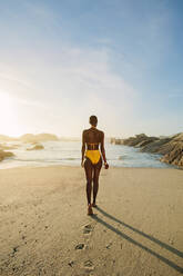 Rückansicht einer afrikanischen Frau im gelben Bikini, die ins Meer geht. Frau, die an einem Sommertag in Badekleidung zum Meer geht. - JLPSF14845