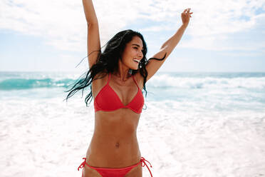 Happy young woman in bikini dancing on the beach. Caucasian female model enjoying herself on the sea shore. - JLPSF14866
