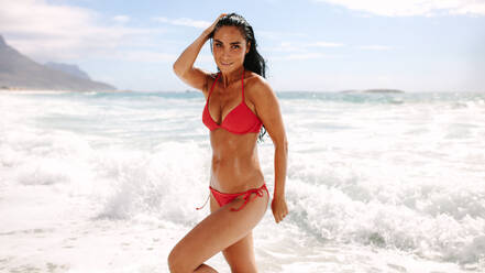 Portrait of sensuous bikini model standing on the beach. Beautiful young woman posing in swimsuit on the sea shore. - JLPSF14869