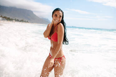 Cheerful woman standing at the beach. Female in bikini enjoying getting wet in sea water. - JLPSF14870
