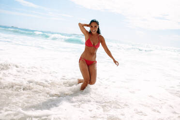 Teenage girls wearing a pink bikini running along a sandy beach by