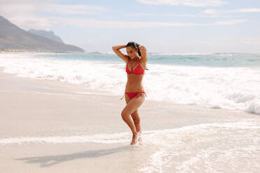 Full length of woman coming out of sea after a swim. Female in bikini walking along the beach. - JLPSF14875