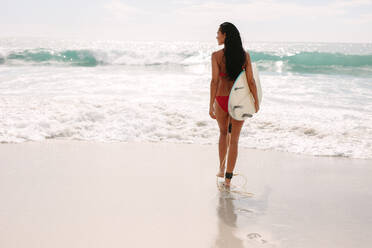 Rückansicht einer jungen Frau, die mit einem Surfbrett zum Meer geht. Eine Frau geht an einem Sommertag zum Surfen - JLPSF14877