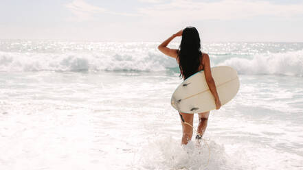 Rückansicht einer Frau mit Surfbrett, die ins Meer geht. Kaukasische Frau, die ein Surfbrett hält, um im Meer zu surfen. - JLPSF14878