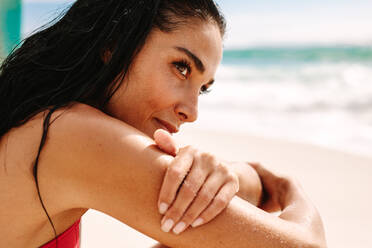 Close up of beautiful woman sitting on the beach and looking away. Female model relaxing on the sea shore on a summer day. - JLPSF14891