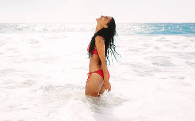 Woman in bikini standing in sea water and having fun. Female enjoying her summer holidays at the beach. - JLPSF14894