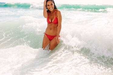 Woman in bikini standing in the water at the shore enjoying the sea waves. Woman on vacation having fun at the beach. - JLPSF14900