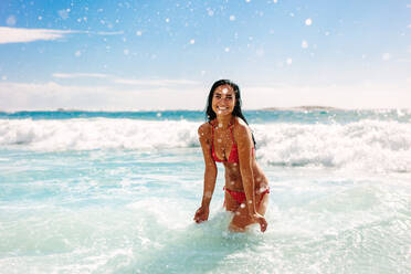 Woman on vacation having fun at the beach playing in the water. Female in bikini enjoying splashing water at the beach. - JLPSF14901