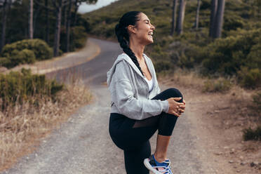 Fitness-Frau dehnt ihr Bein vor einem Lauf. Weibliche Läuferin macht Stretching-Training im Freien und lächelt. - JLPSF14903