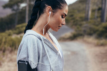 Seitenansicht einer Sportlerin mit Kopfhörern: Frau hört Musik beim morgendlichen Training im Freien. - JLPSF14907