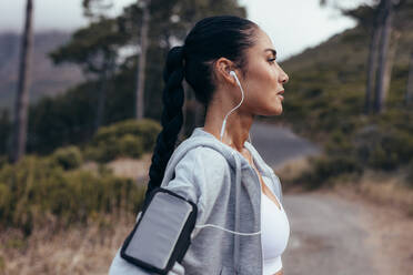 Seitenansicht einer Fitness-Frau, die im Freien steht. Sportliche Frau mit Smartphone-Armband, die sich nach dem Outdoor-Training ausruht. - JLPSF14908