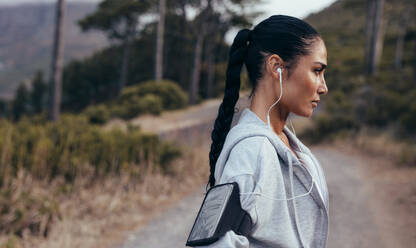 Seitenansicht einer sportlichen Frau, die sich nach dem Training im Freien ausruht. Fitness-Frau mit Handy-Armband, die sich nach dem Outdoor-Training ausruht. - JLPSF14915