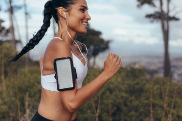 Seitenansicht einer Fitness-Frau, die morgens im Freien sprintet. Weibliche Athletin mit Handy-Armband und Kopfhörern am Morgen. - JLPSF14923