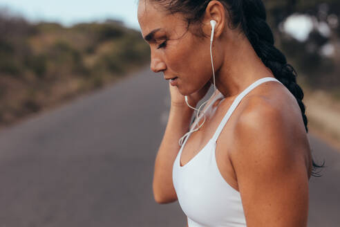 Seitenansicht einer Sportlerin mit Kopfhörern, die beim Training Musik hört. Sportlerin, die morgens im Freien Musik hört. - JLPSF14929