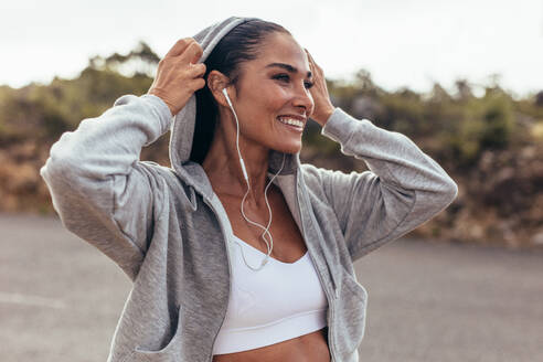 Fitness woman wearing a hooded shirt walking outdoors. Smiling female on early morning walk. - JLPSF14939