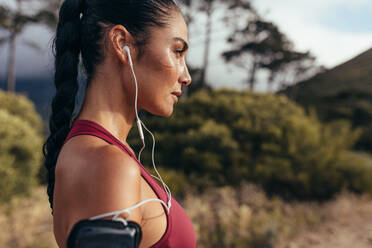 Seitenansicht einer Sportlerin mit Kopfhörern, die im Freien steht. Frau hört Musik beim morgendlichen Training. - JLPSF14941