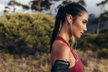 Seitenansicht einer Fitness-Frau, die im Freien steht und zum Morgenlauf bereit ist. Eine Sportlerin mit Kopfhörern macht eine Pause vom Laufen. - JLPSF14942