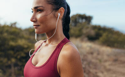 Seitenansicht einer Sportlerin mit Kopfhörern, die vor einem Lauf im Freien steht. Eine Läuferin hört beim morgendlichen Training Musik. - JLPSF14945