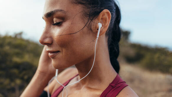 Hübsche junge Frau trägt Kopfhörer, um Musik zu hören, bevor sie ihr Lauftraining beginnt. Fitte Sportlerin vor ihrem Lauf im Freien. - JLPSF14946