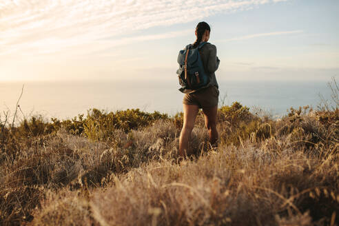 Rückansicht einer Frau, die auf einem Bergpfad wandert. Frau, die mit einem Rucksack auf einem felsigen Hügel wandert. - JLPSF14948