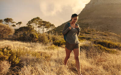 Young woman with backpack walking down the meadow. Female hiking alone in nature. - JLPSF14950