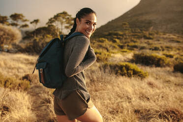 Woman with backpack walking up the country trail and looking over her shoulder and smiling. - JLPSF14958