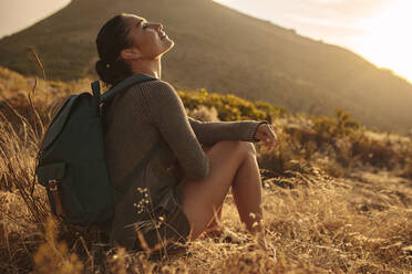 Young woman hiking in countryside sitting and taking rest. Female hiker resting on dry grass field. - JLPSF14962